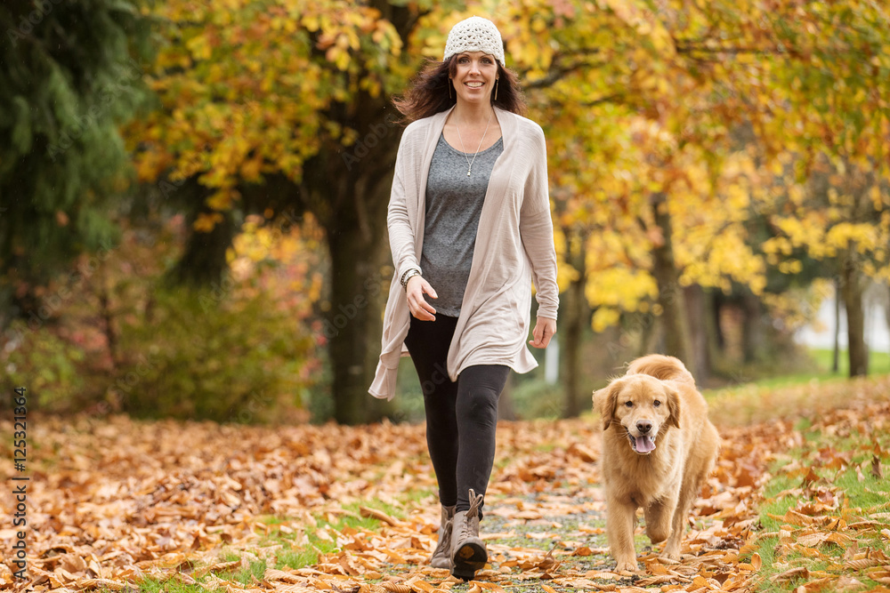 Happy woman walking her Golden Retriever Dog in a park with Fall Happy woman walking her Golden Retriever Dog in a park with Fall