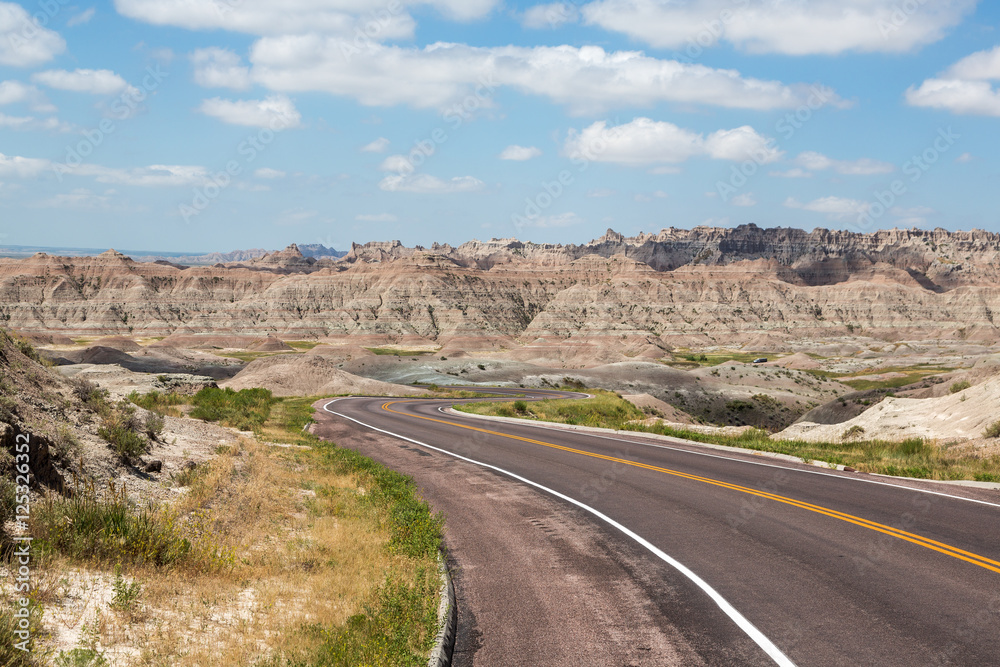 A road cutting through rolling hills in the Badlands of South Dakota on a summer day.