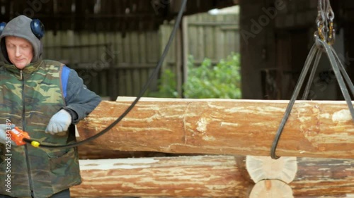 Builder raises wooden timber with Overhead Winch Crane. A man holds a log and transfer it to the future home