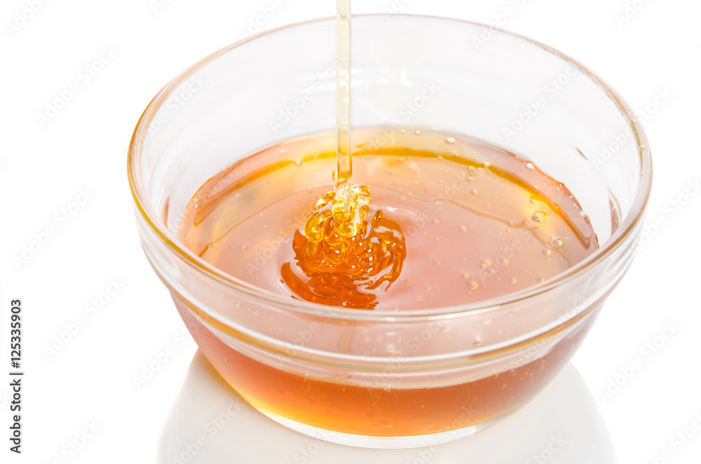 Honey dripping into glass bowl isolated on white background