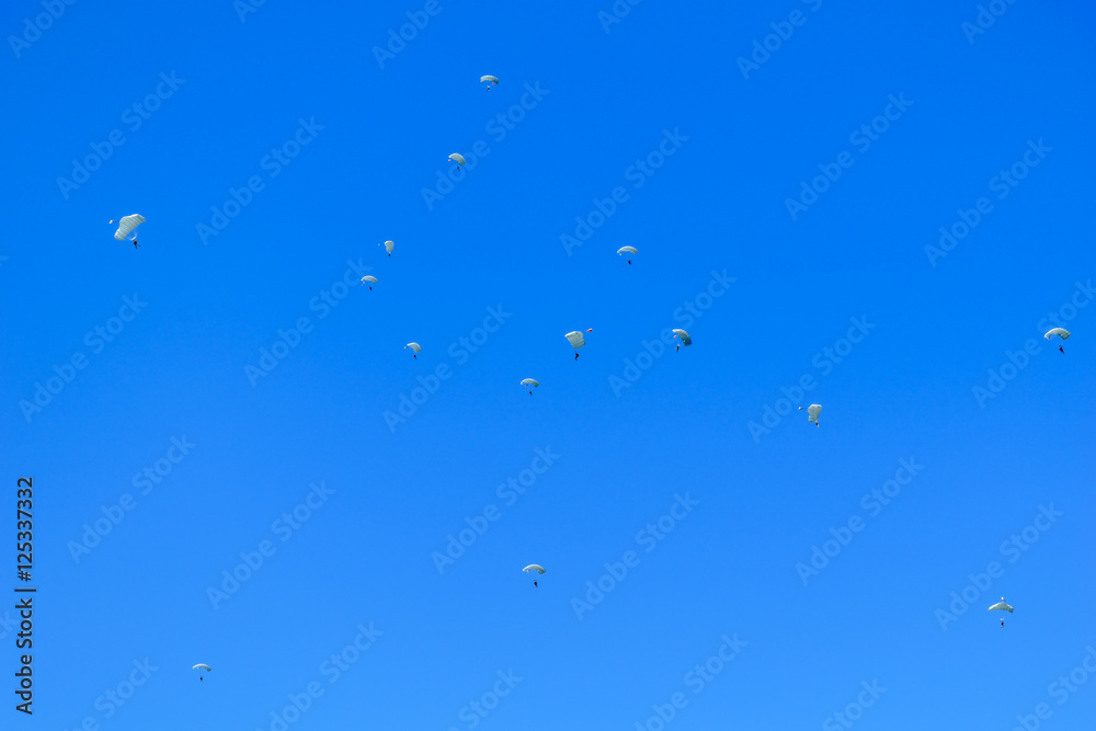 Paratroopers descend to earth on the blue clear sky background