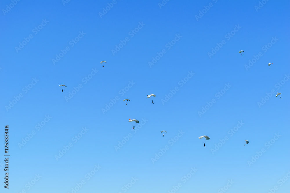 Paratroopers descend to earth on the blue clear sky background