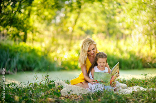 Obraz na płótnie mother reads the book in the daughter on a grass w salonie