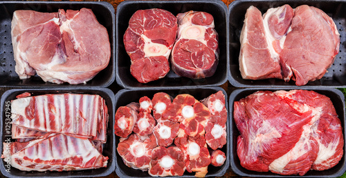 Different types of raw meat in plastic boxes, lamb shank on the