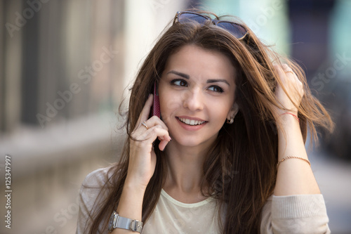 Happy young woman talking on mobile phone at city street lifestyle portrait.
