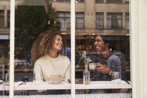 View Through Window Of Couple Enjoying Drink In Coffee Shop