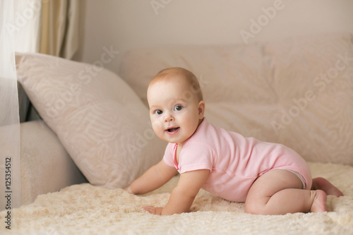 Cute smiling baby in pink bodysuit on a beige couch