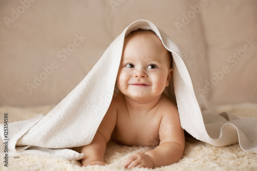 Cute smiling baby covered with white towel on a beige couch