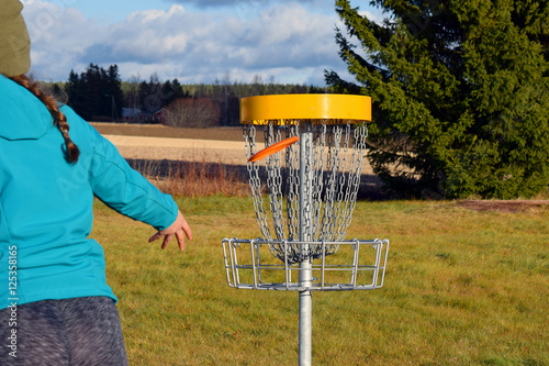 Young woman throws disc to target on disc golf course.