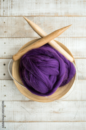 wooden knitting needles and purple merino wool ball in a basket