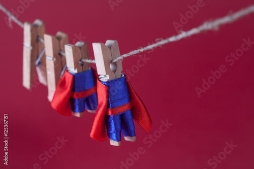 Super team leadership concept photo with clothespin superheroes in blue suit and red cape. Big small powerful heroes hanging clothesline. Pink background. macro view