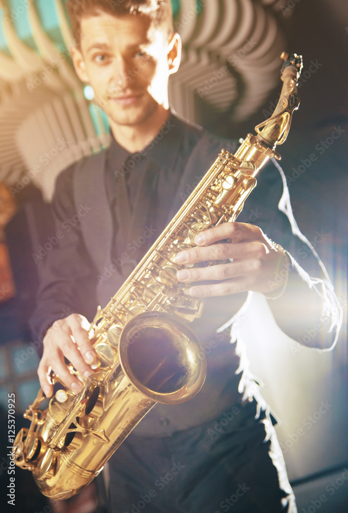 Obraz premium A young man in a suit standing with a saxophone musical instrument