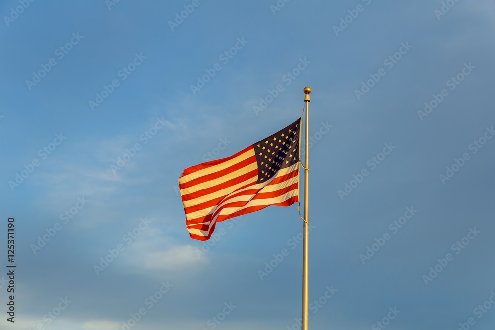 American flag on flagpole waving in the wind against clouds, blue sky and the moon American flag on flagpole waving in the wind against clouds, blue sky and the moon
