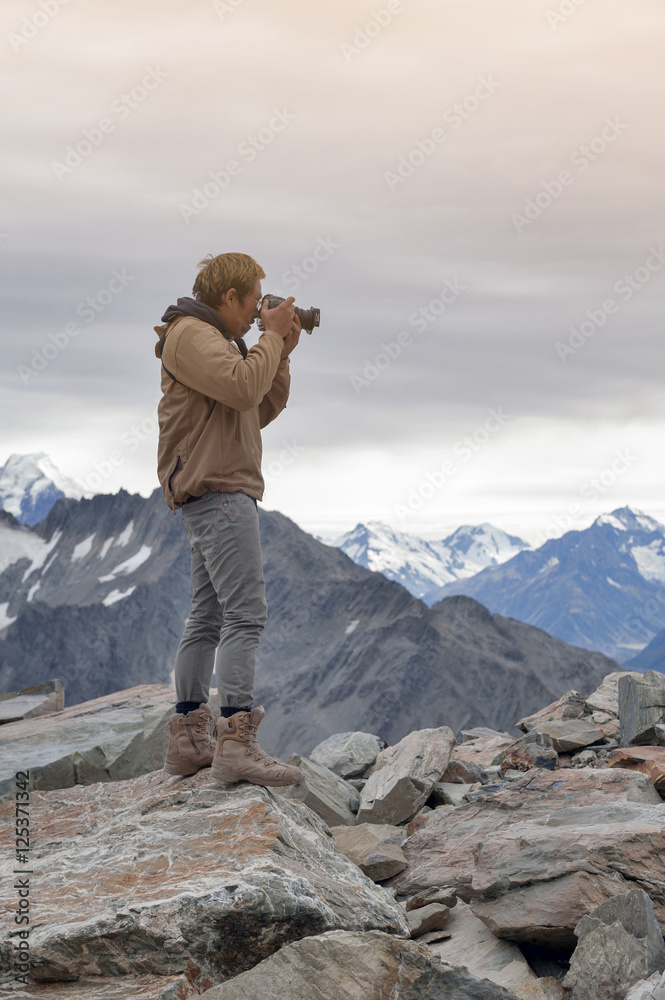 Male model posts at the top of snowcapped mountain peak around Aoraki Mount Cook and Mount Cook National Park