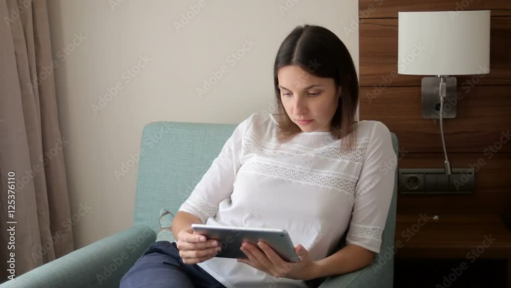 young girl is sitting on a chair with the tablet in the room young girl is sitting on a chair with the tablet in the room