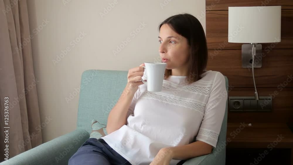 young girl sitting on chair and drinking tea from a mug in the room young girl sitting on chair and drinking tea from a mug in the room