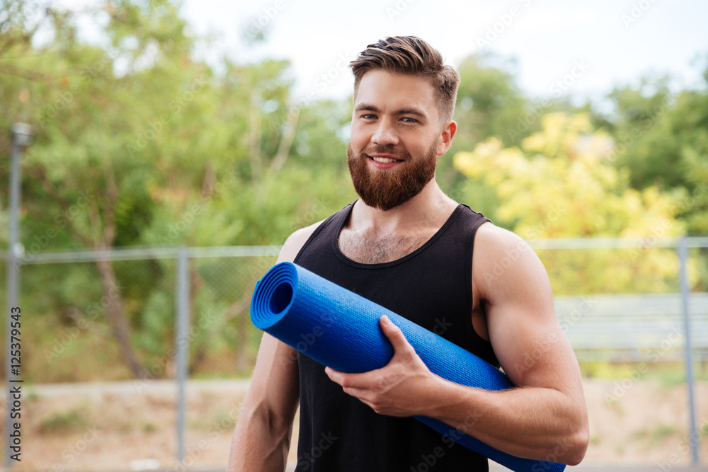 Handsome bearded young sportsman holding yoga mat Handsome bearded young sportsman holding yoga mat