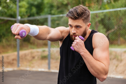 Young bearded sports man doing workout with small dumbbells