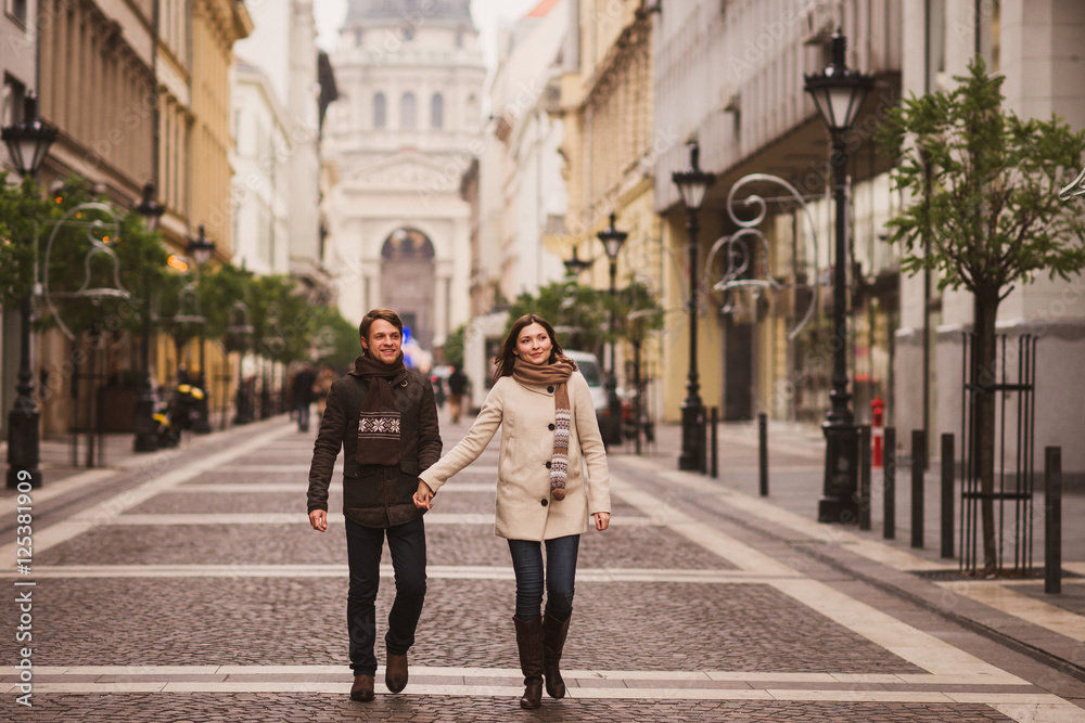Christmas in old town. Young cheerful caucasian couple in warm cozy clothes walking in city centre.