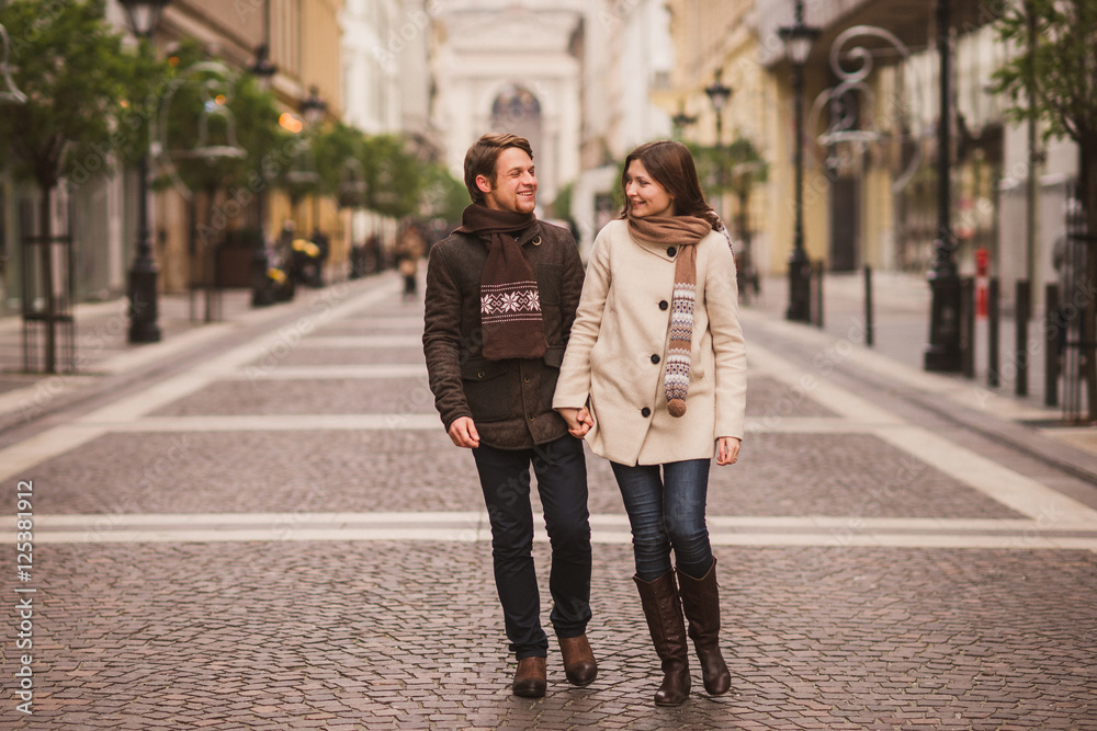 Christmas in old town. Young cheerful caucasian couple in warm cozy clothes walking in city centre.