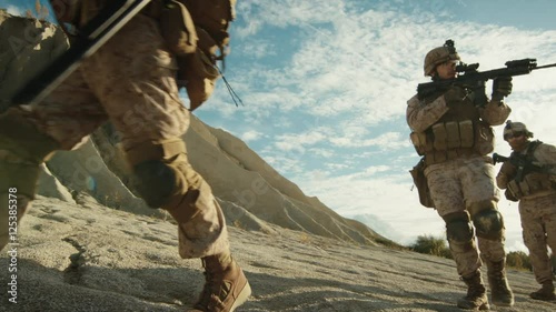 Squad of Fully Equipped and Armed Soldiers Walking in Single File in the Desert. Slow Motion.