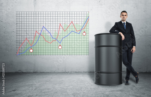 Businessman in confident pose standing next to oil barrel on background of graph photo