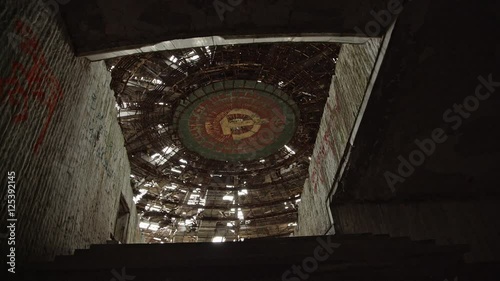 Camera tracks to the entrance of the main auditorium at the ruined Buzludzha monument in Bulgaria, showing the Soviet hammer and sickle