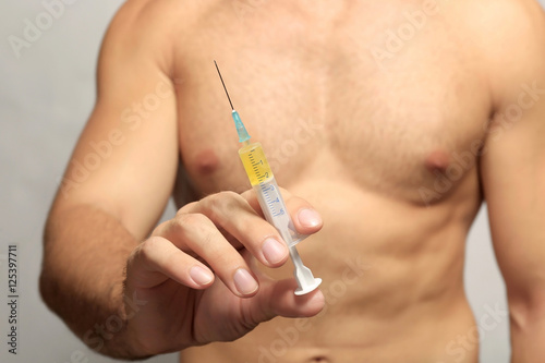 Muscular man holding syringe, closeup