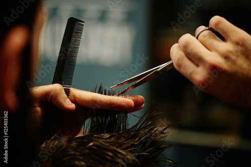 Hands of a Barber the man in the process of cutting hair with scissors in Barbershop closeup