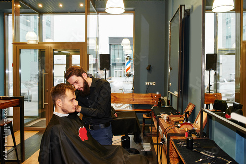 The Barber man in the black shirt in the process of cutting a customer in the barbershop © amixstudio