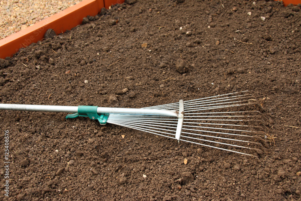 Soil alignment with a lawn rake on a modern plastic raised garden vegetable bed in the summer garden