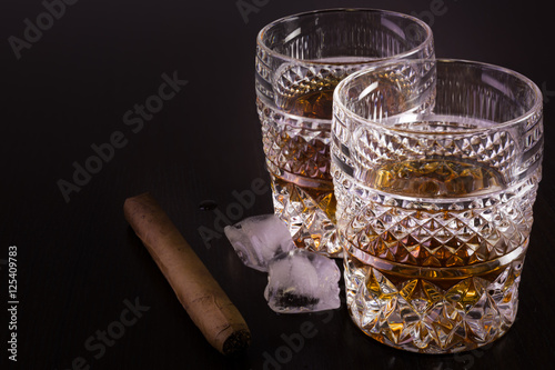 Two glasses of whisky, ice cubes and a cigar on black