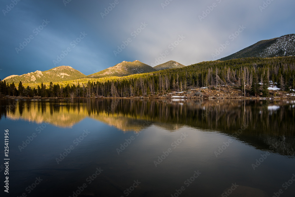 Mountains and trees reflected in a calm lake.