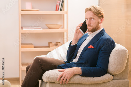 Hnadsome rich European businessman using mobile or smart phone for talking with foreing business partners concerning new conceptions, strategies. photo