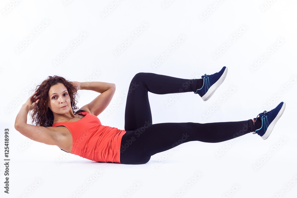 Pretty brunette in active wear is doing abdominal exercises on white background. Pretty brunette in active wear is doing abdominal exercises on white background.