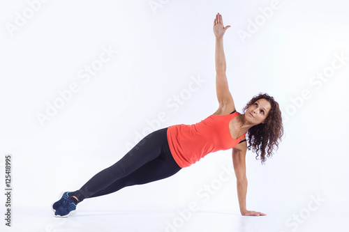 Pretty brunette in active wear is doing yoga on white background.