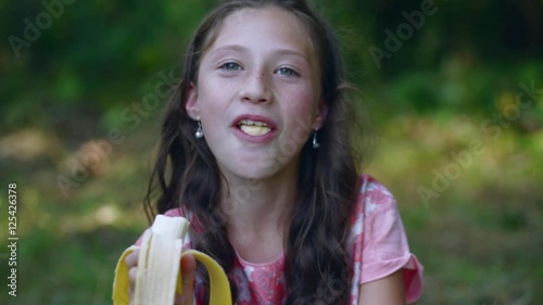 Beautiful little girl eating a banana in the garden