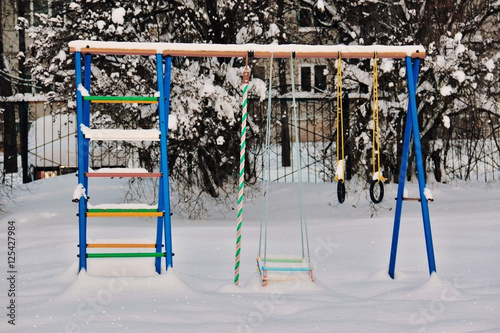 Baby swings in snow in city park in deep winter