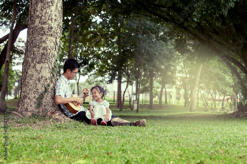 Father and child having fun to play guitar together in the park