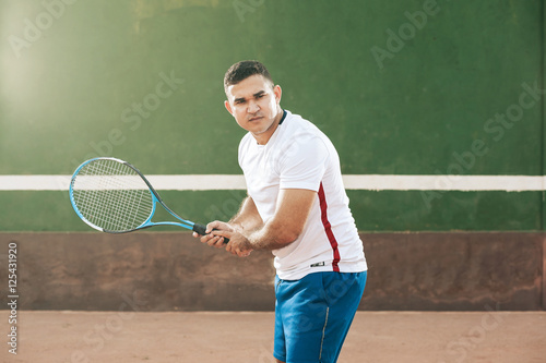 Handsome young man on tennis court. Man playing tennis. Man is ready to hit tennis ball
