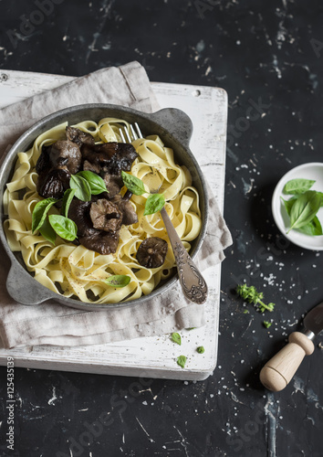 Italian pasta tagliatelle with wild mushrooms in a frying pan on a dark background. Delicious vegetarian food