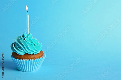 Fresh tasty cupcake with candle on blue background