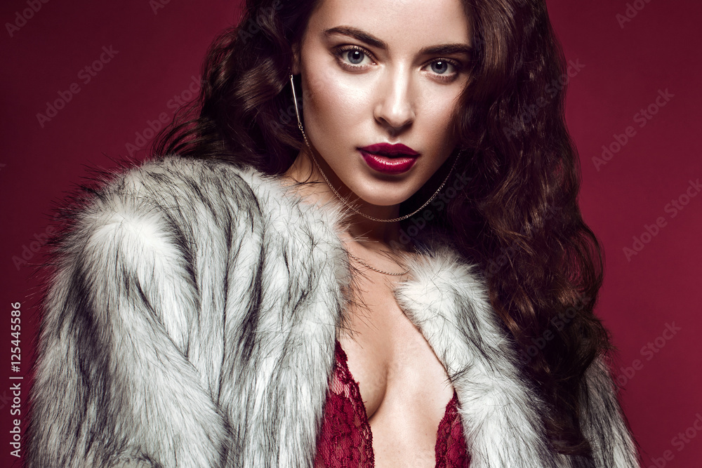 Beautiful sexy long-haired brunette woman in red lingerie and fur coat posing in the studio. The beauty of the face and body. Photos shot in a studio