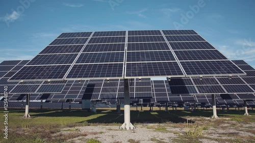 Multiple sets of large solar panel arrays facing upward to a deep blue sky from ground photo