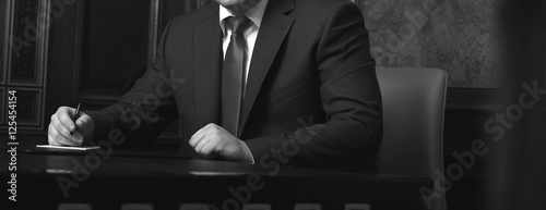 Close up of businessman sitting at table and signing document, black and white photo