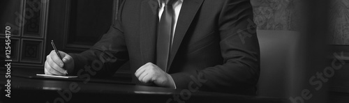 Close up of businessman sitting at table and signing document, black and white photo
