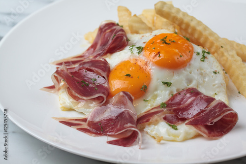 Appetizing Spanish Iberian cured ham with fried egg and chips on