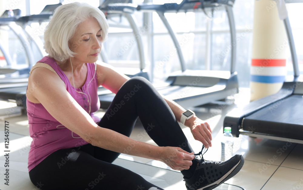 Pretty gray haired woman tying shoelaces in a gym.