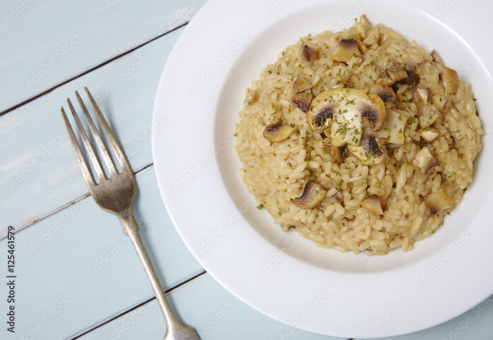 A dinner dish of mushroom and chicken risotto rice on a painted wooden table top background A dinner dish of mushroom and chicken risotto rice on a painted wooden table top background