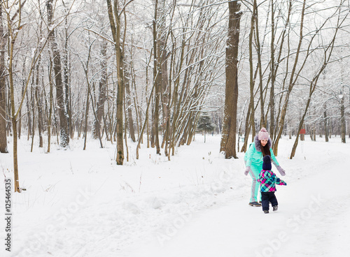 Mother and little toddler girl walking in the winter forest and having fun with snow. Family enjoying winter. Christmas and lifestyle concept.